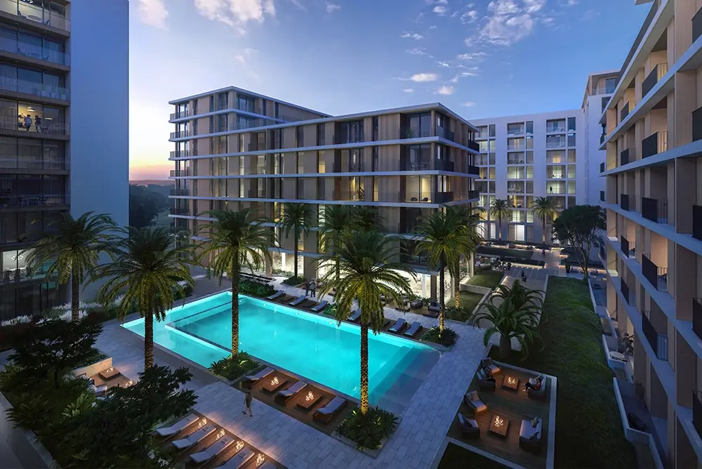 Modern resort at dusk featuring a large illuminated swimming pool, palm trees, and contemporary multi-story buildings. Modern resort at dusk featuring a large illuminated swimming pool, palm trees, and contemporary multi-story buildings.