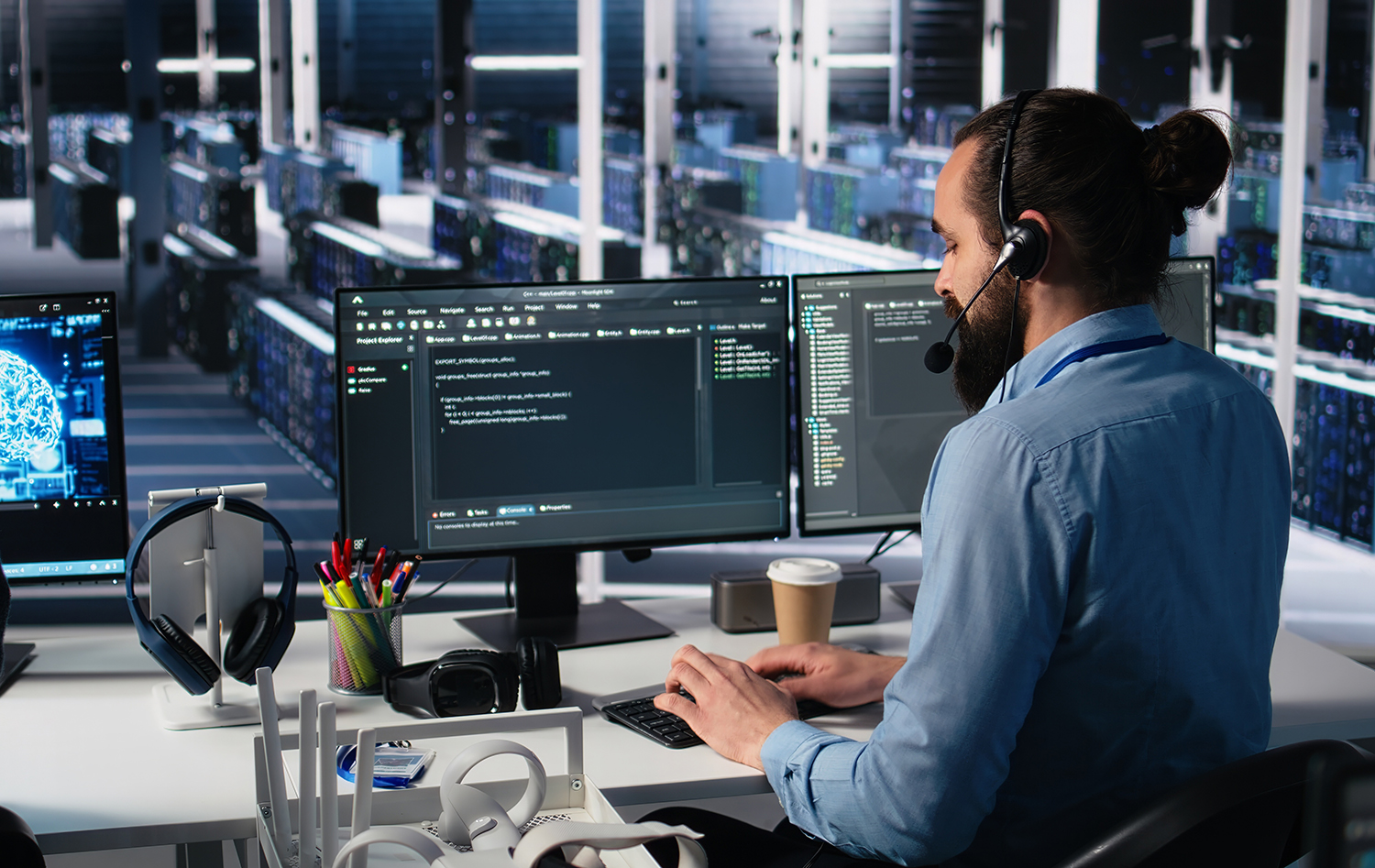 An IT support technician wearing a headset works across multiple monitors displaying code and development environments in a dark, server-lined workspace. An IT support technician wearing a headset works across multiple monitors displaying code and development environments in a dark, server-lined workspace.